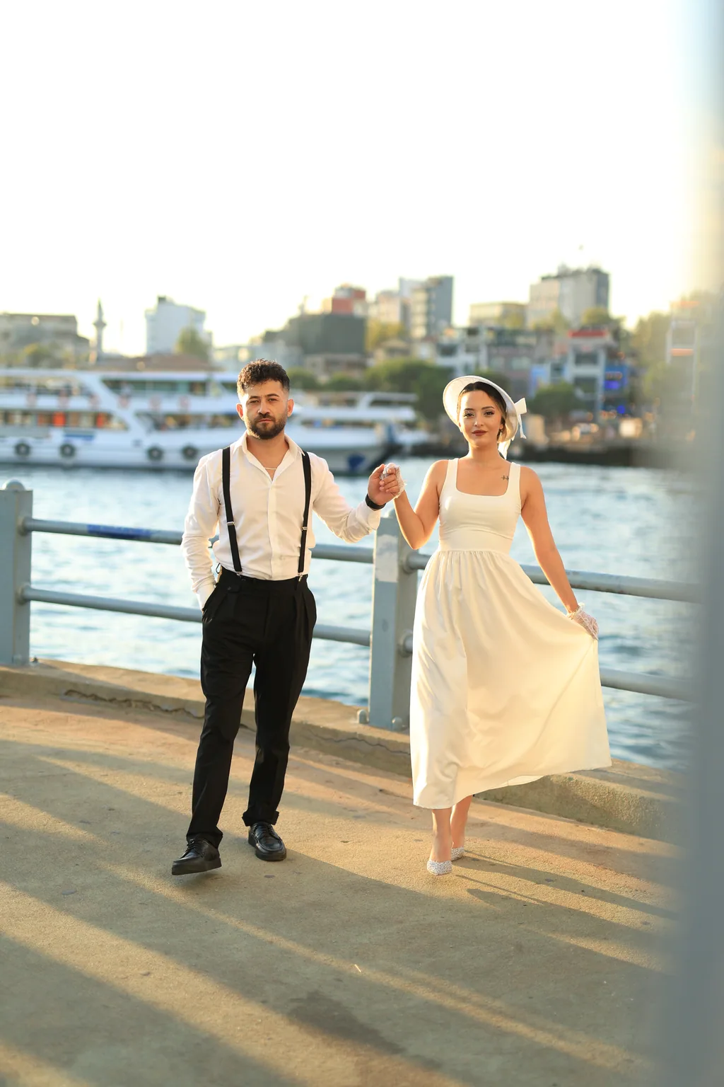 Gelin ve damat Boğaz kıyısında el ele yürüyor; arkada vapurlar.