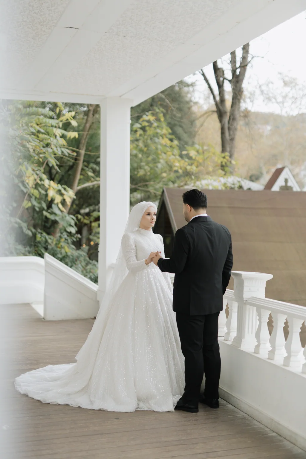 Duvaklı gelin ve damat, beyaz sütunlu bir terasta karşı karşıya duruyor.